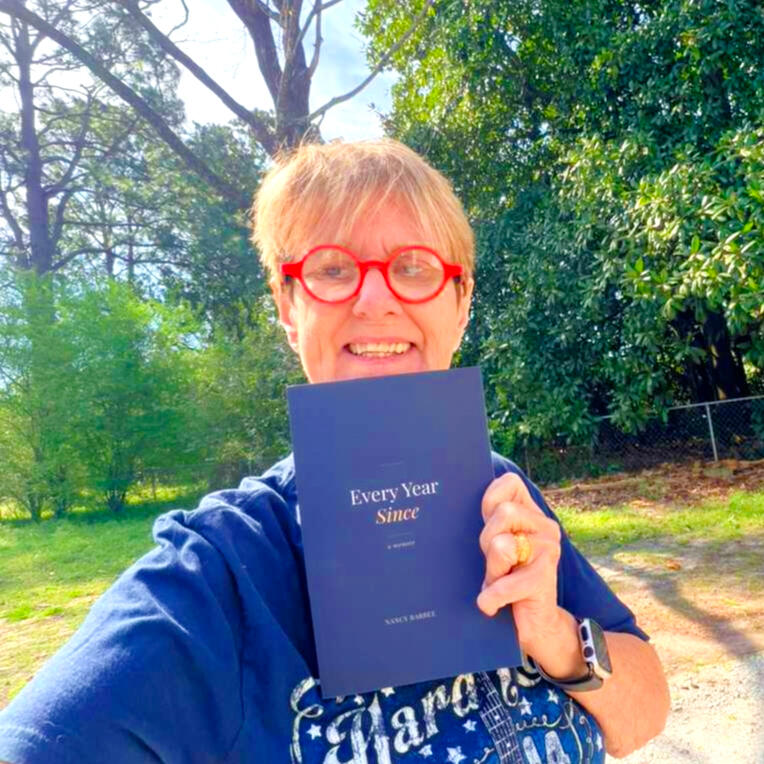 Nancy Barbee, author of Every Year Since, smiling and holding her memoir outdoors in North Carolina.